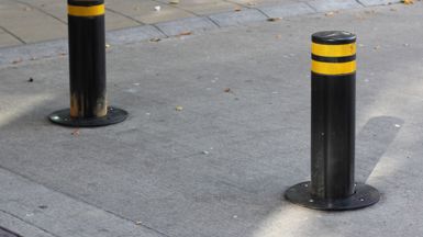 Two round black bollards about one metre apart on a road, each with two stripes of yellow reflective tape at the top