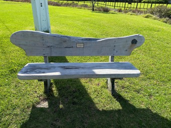 Wooden bench sitting on grass with a small golden plaque in the middle.