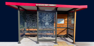 Waiheke bus shelter with a red roof, wooden seat and glass featuring a Maori design.
