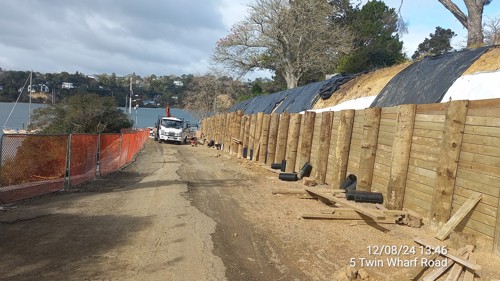 Timber piles and lagging on the top of the piles. A truck is shown working on the wall installation in the background.