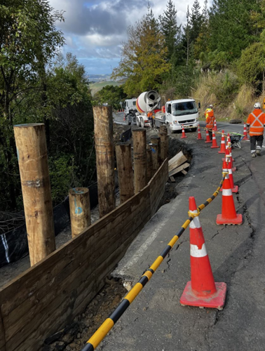 Work crew and cement truck laying cement at roadside slip marked with orange cones
