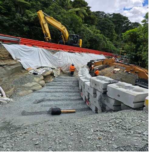 A concrete block wall is being created to the right of the image. Behind the wall, the team are backfilling and compacting as they go.