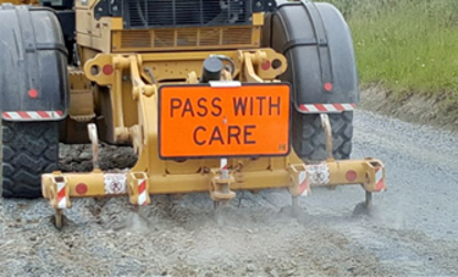 Tractor on a gravel road with an orange "pass with care" sign
